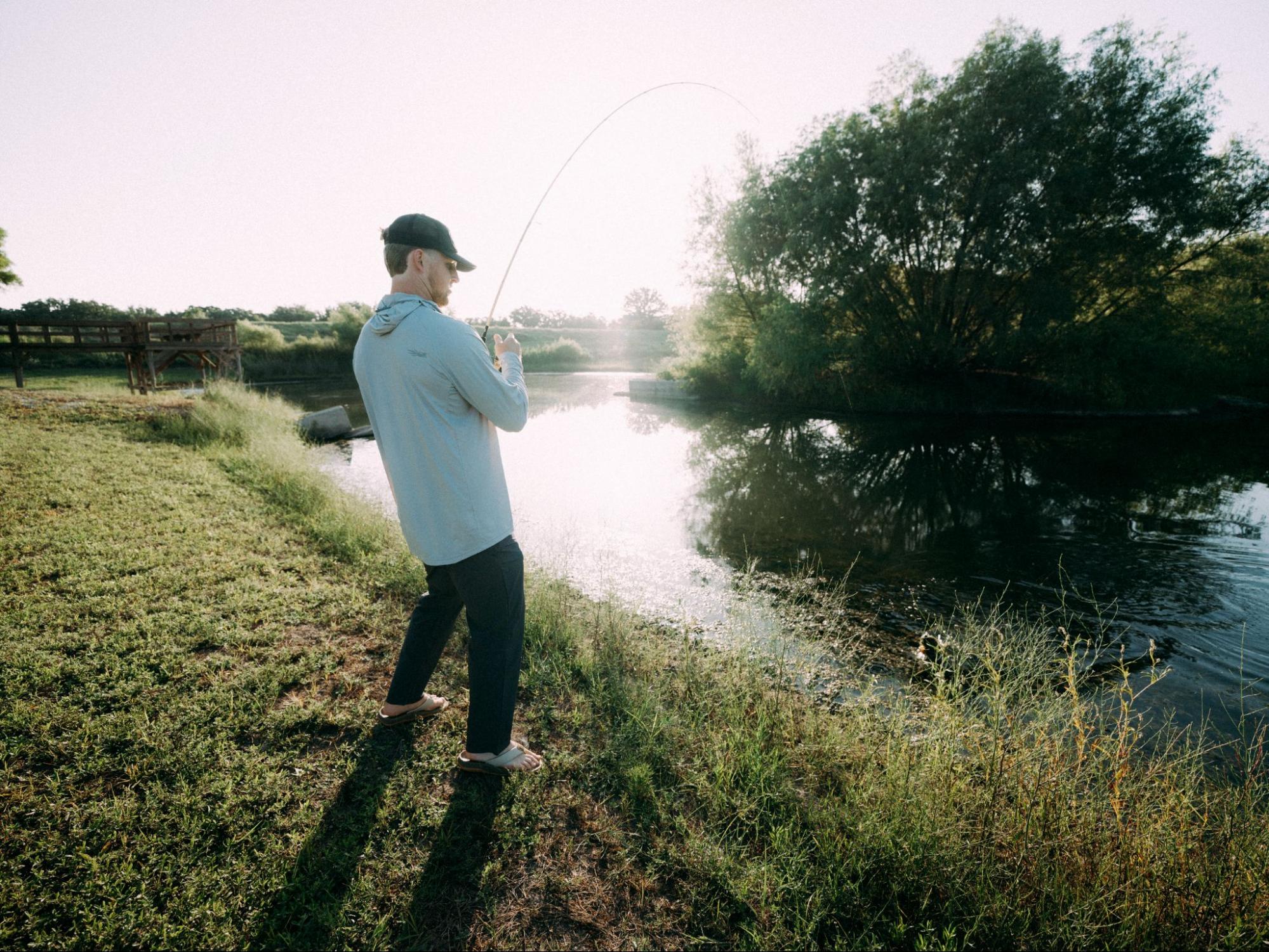 Cooper holding a fishing rod on a grassy bank fishing for largemouth bass